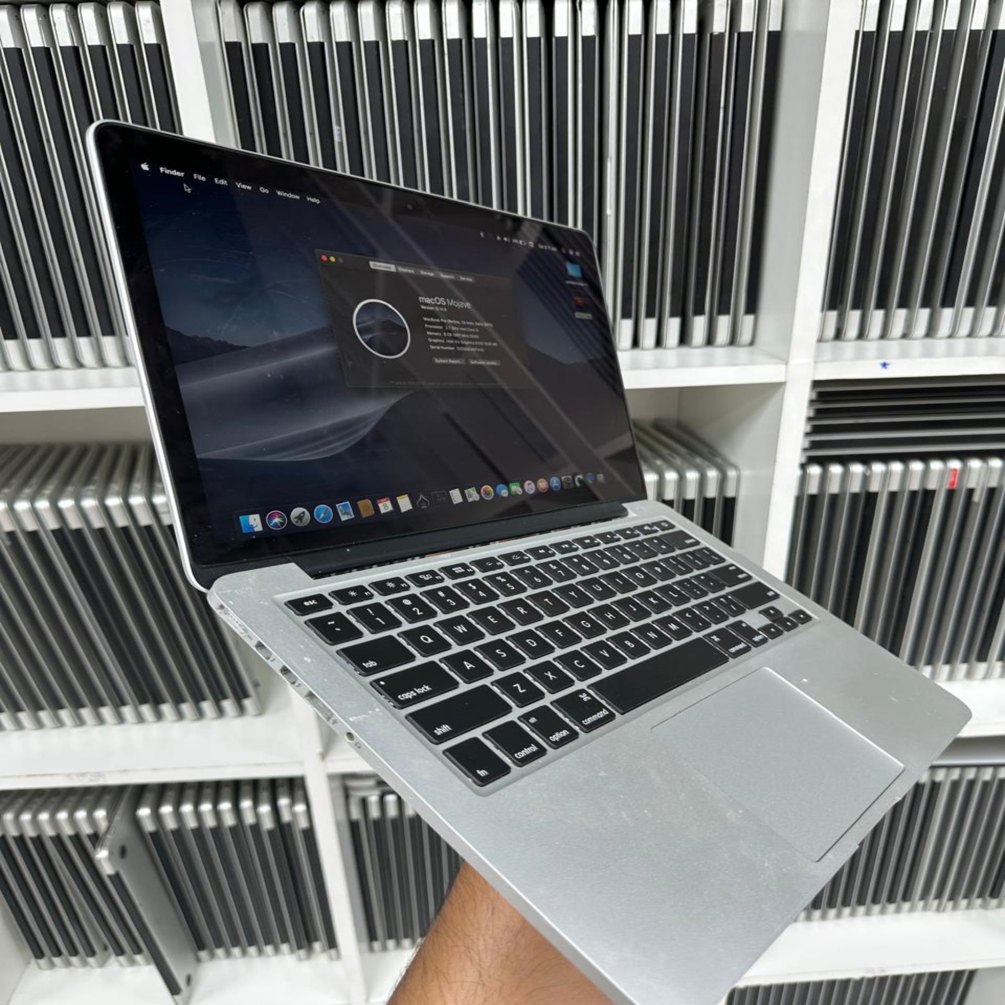Laptop held in front of a shelf with multiple laptops