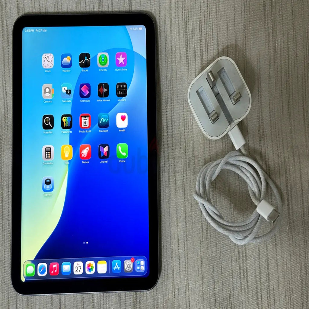 Tablet with app icons displayed on screen next to a charging cable and adapter on a wooden surface